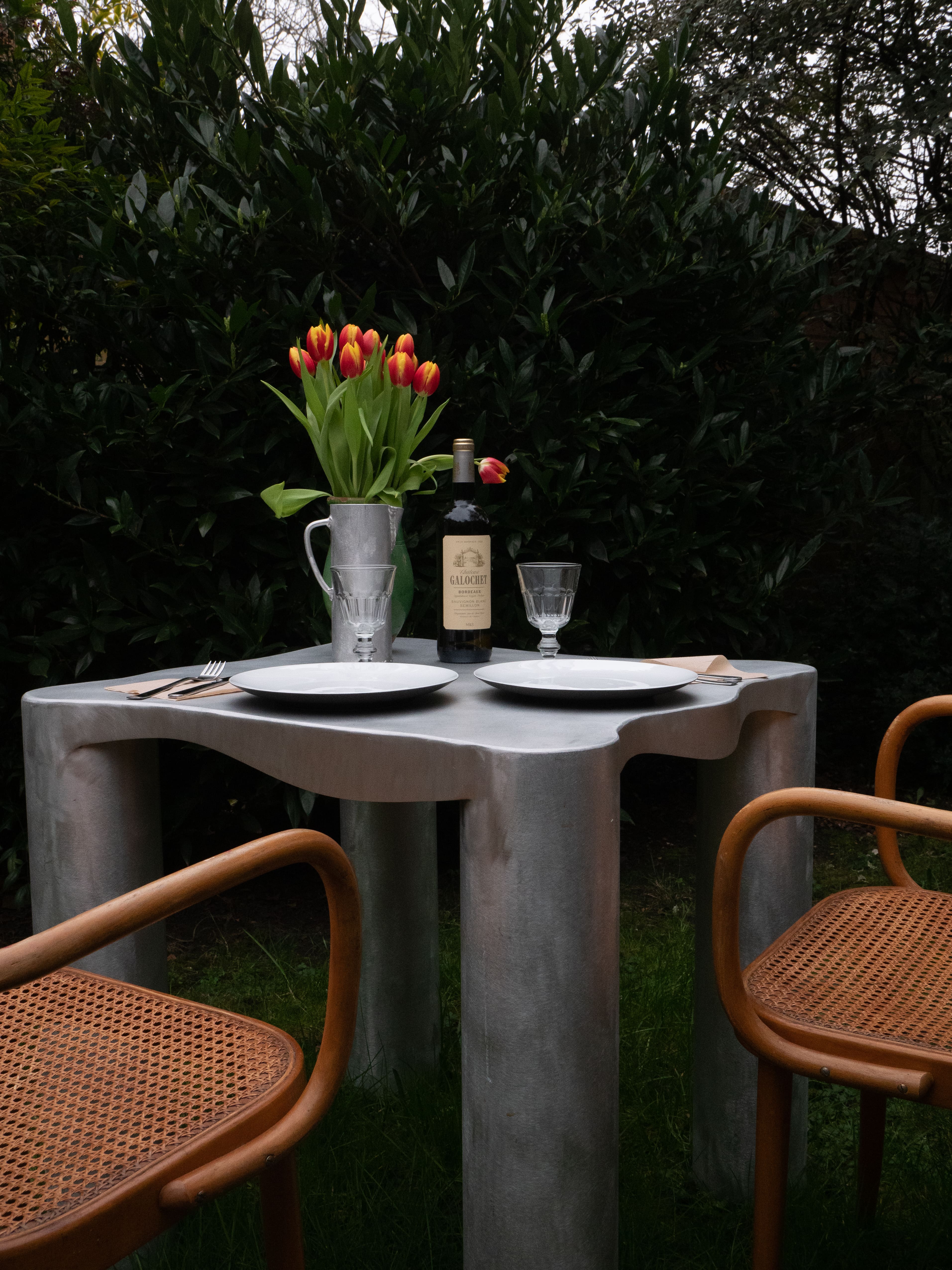 Silver aluminium dining table with organic wavy edges and integrated legs made of concrete
