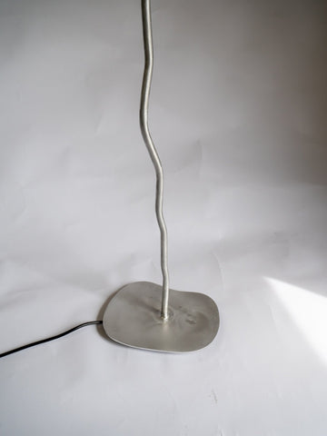 A sleek silver-toned aluminium pea head floor lamp with a wavy metal stem and flat circular base