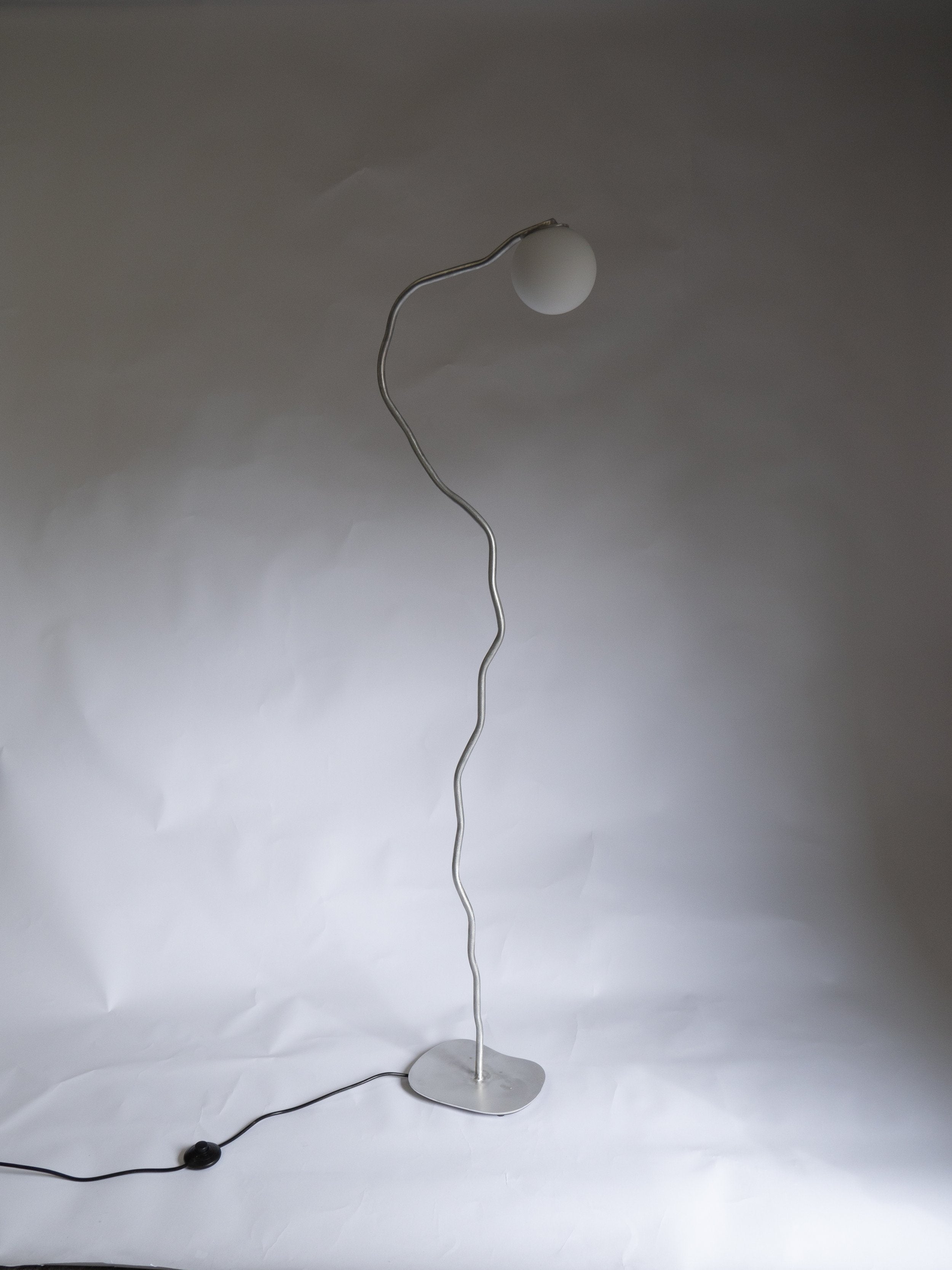 A sleek aluminium pea head floor lamp with a wavy silver metal stem and matte white spherical shade