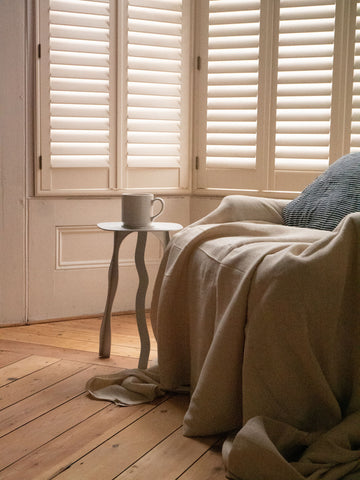 Cream-colored ceramic mug resting on a small aluminum side table with a simple handle and sleek design