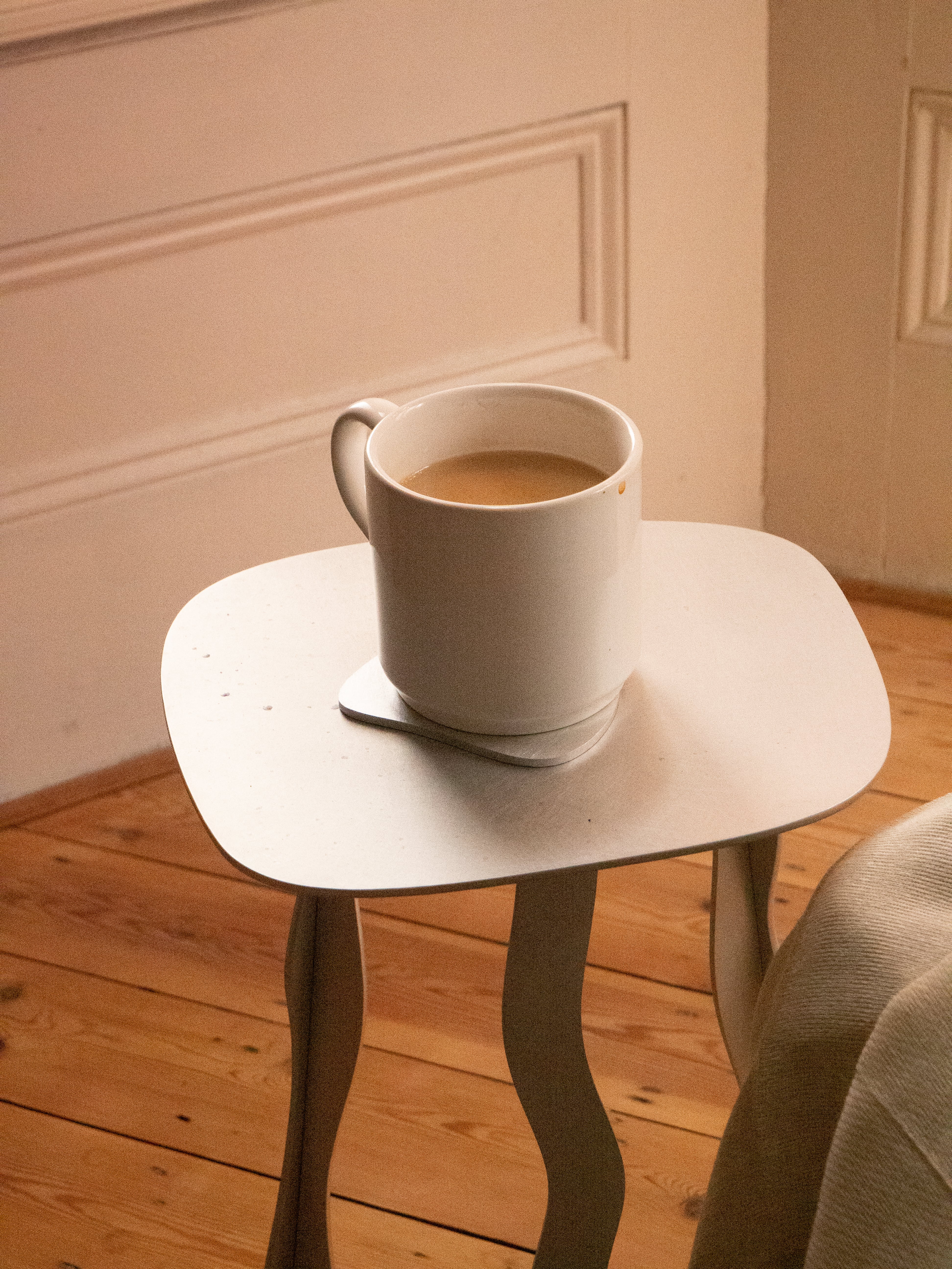 White aluminium side table with minimalist design holding a white ceramic coffee mug filled with light brown beverage