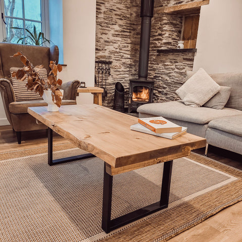 A rustic light wood waney edge coffee table with black metal square legs perfect for any living room setup