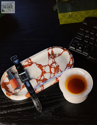 Amaryllis marble tray with white and orange pattern holding a black leather watch and orange lipstick with sleek design