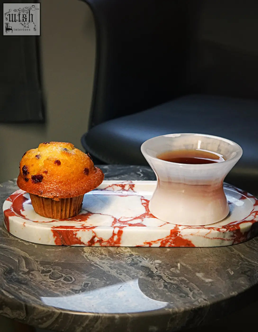 A white and red marble tray with sleek design holds a golden-brown chocolate chip muffin and tapered ceramic teacup