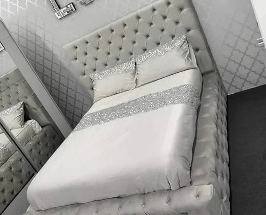 A tufted silver-gray ambassador bed with matching headboard and footboard featuring glittery silver bedding accents