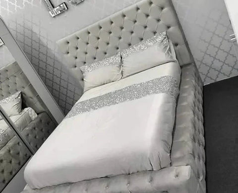 A tufted silver-gray ambassador bed with matching headboard and footboard featuring glittery silver bedding accents