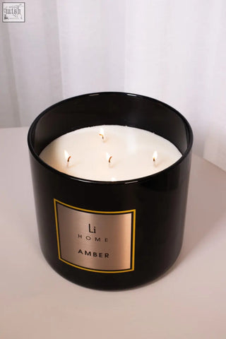 Black cylindrical amber 3 wick luxury candle jar with gold label and four lit white wax candles for large candle collection