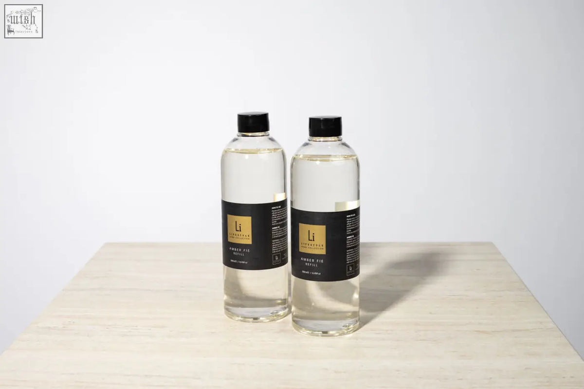 Two clear plastic bottles of l’occitane amber fie premium xxl aromatique diffuser refill with black caps and labels