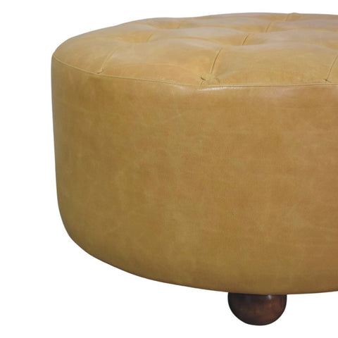 A round mustard yellow tufted leather ottoman with a dark wooden leg perfect for amber oak coffee table setups
