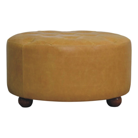 Tan leather tufted ottoman with dark wooden ball feet styled as an amber oak leather coffee table centerpiece