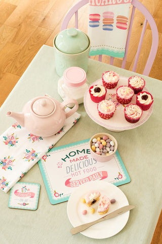 Pink ceramic teapot with matching lid on a floral pattern napkin next to amelie floral pattern cake stand