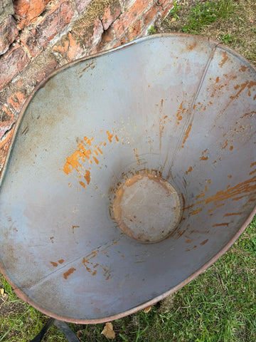 A rusty gray metal vintage french grape hod with orange stains and weathered surface used as log basket planter