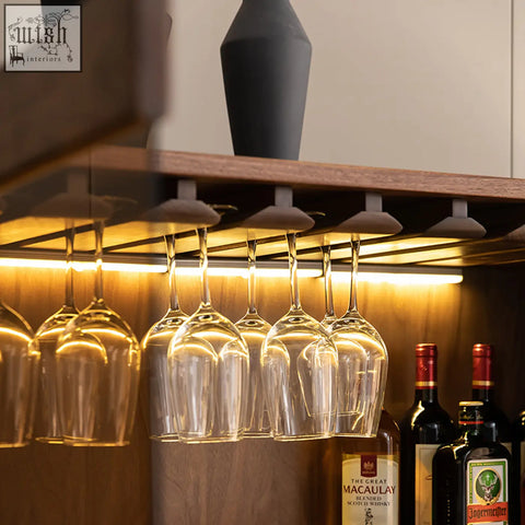 Clear elegant wine glasses with slender stems hang from a solid wood wine rack in the anisimov cabinet wine storage