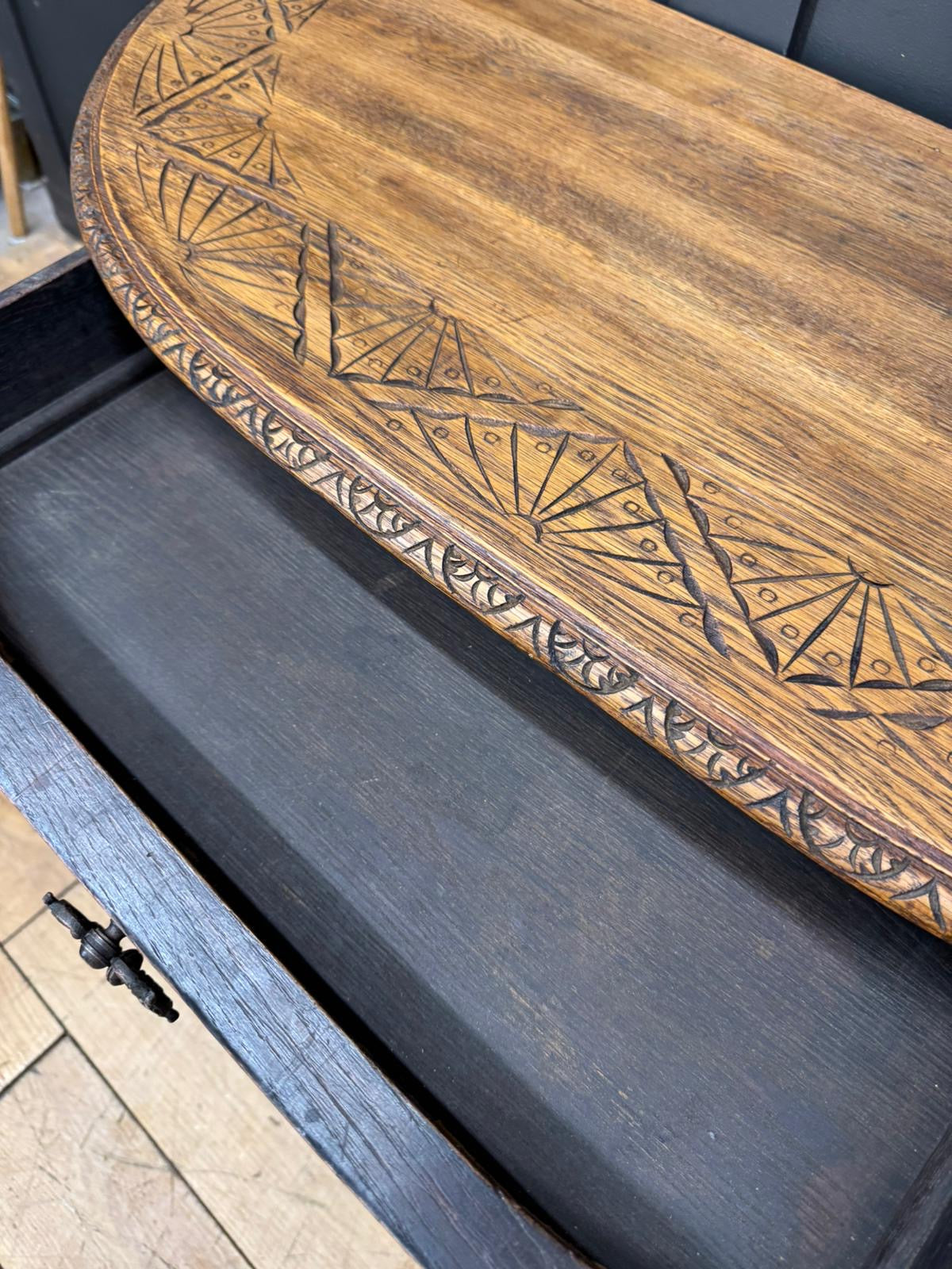 A rustic carved oak console table with warm medium brown finish and intricate geometric carvings on curved edge