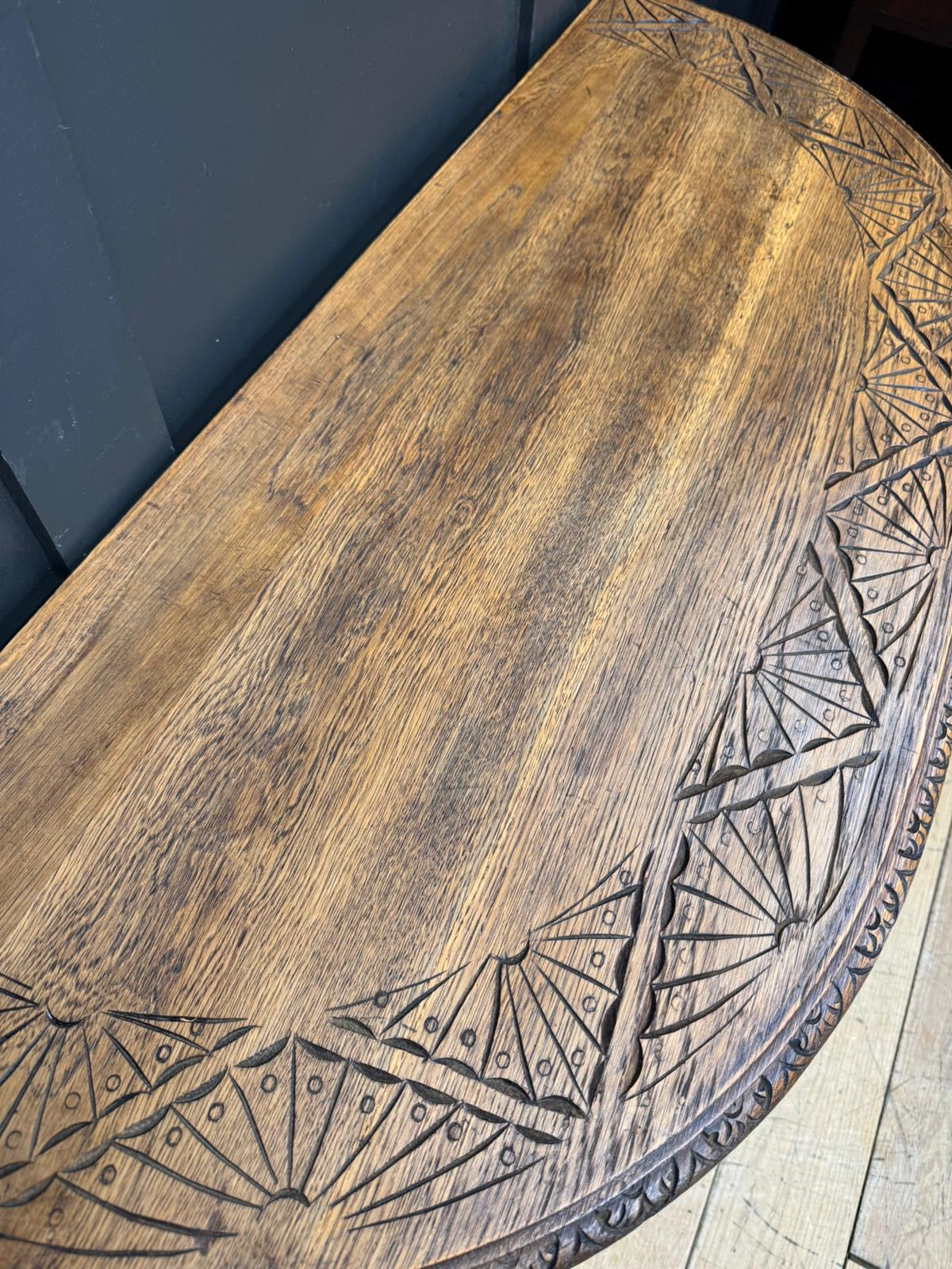 A rustic oval carved oak console table with intricate fan patterns along its curved edge perfect for hallways
