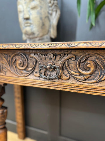 Antique carved oak console table with dark bronze drawer pull and intricate floral carvings for hallway or desk use
