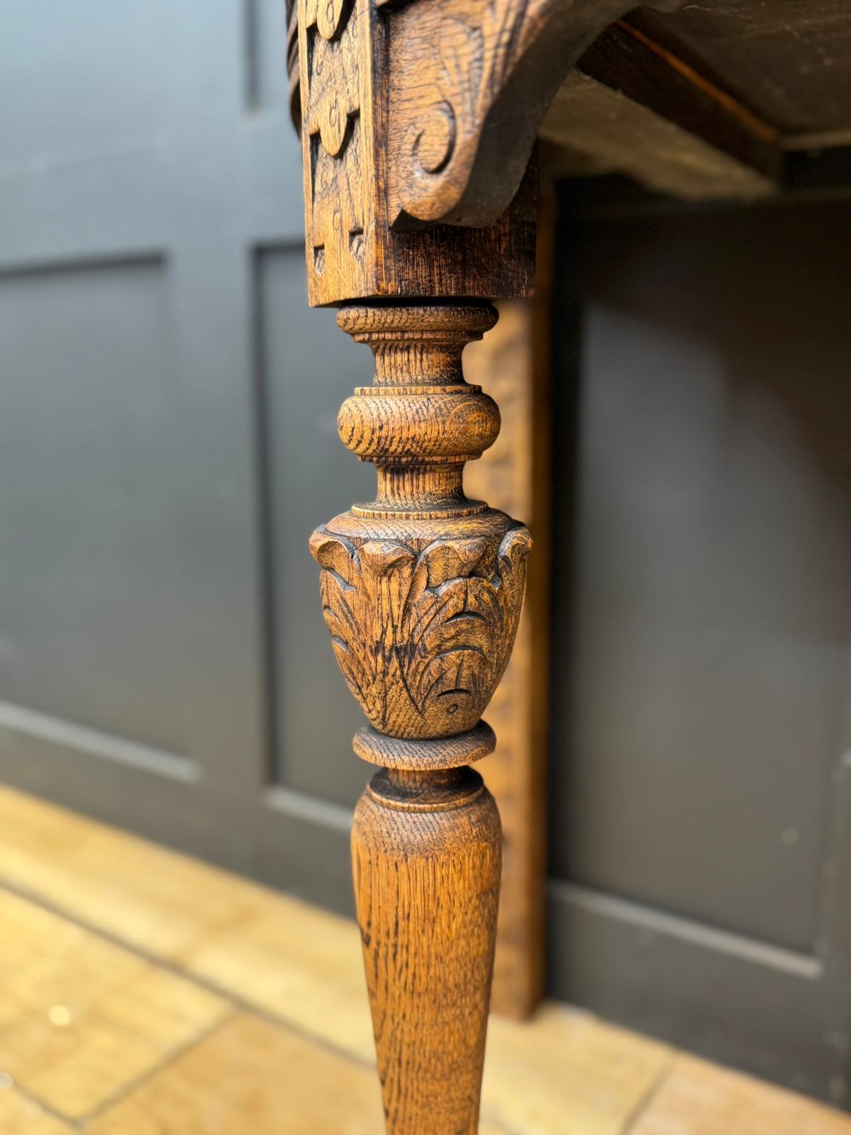 Carved oak leg of an antique console table with intricate floral and scrollwork detailing in oak wood