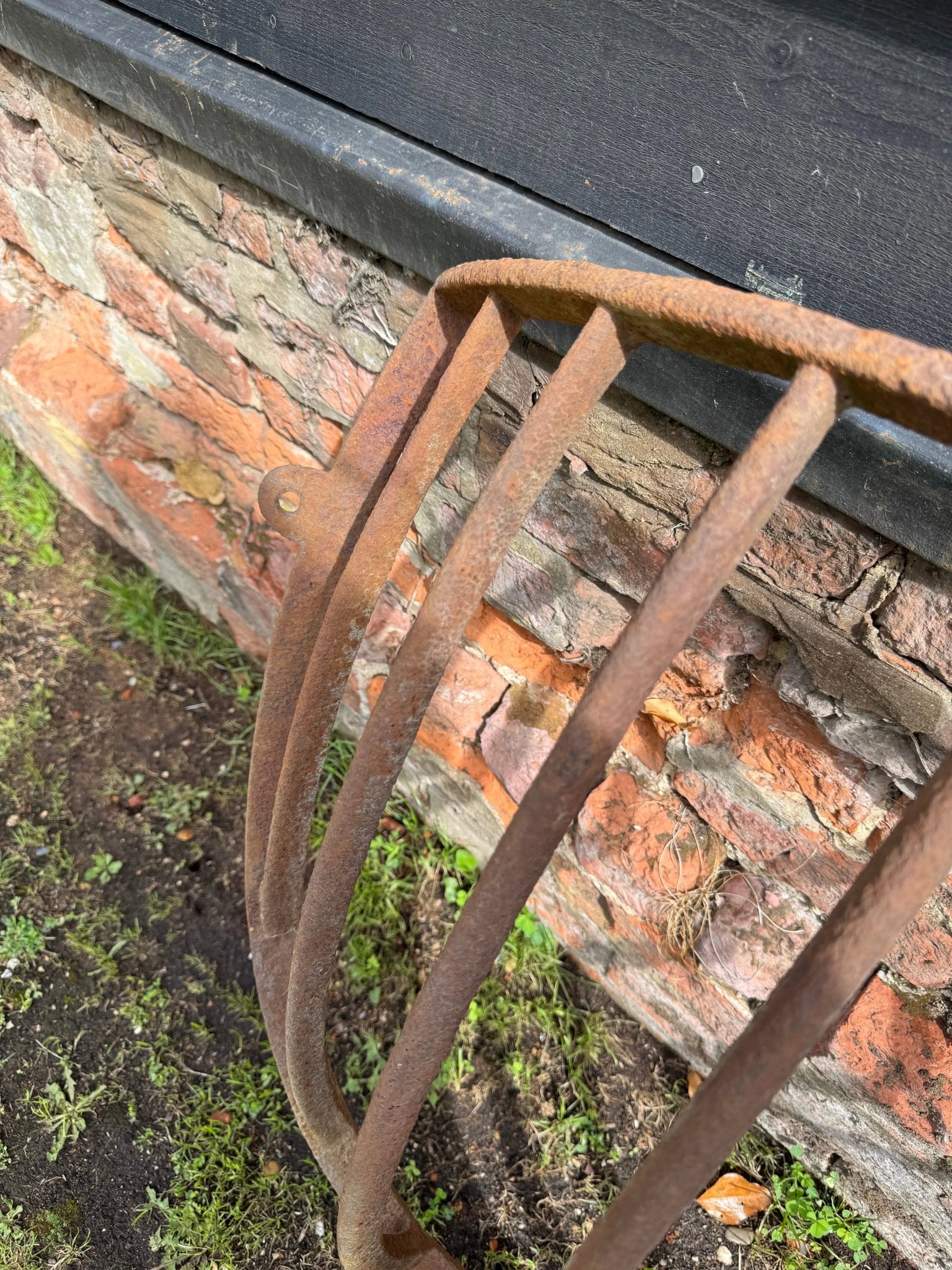 Rusty iron garden rake with curved handle and weathered bars beside antique cast iron corner hay rack planter 81cm