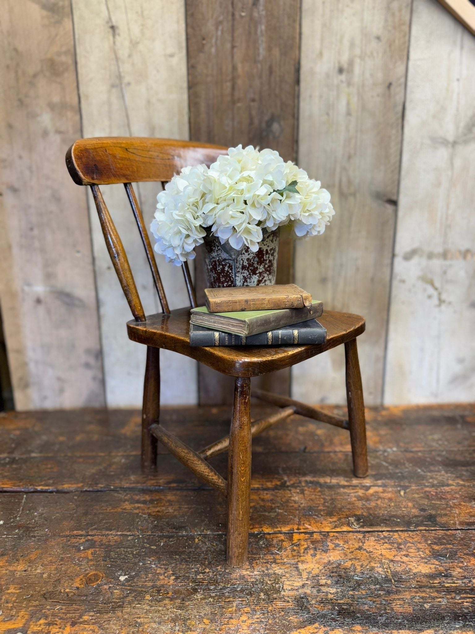 Antique child’s chair with elm seat featuring dark brown wood grain and curved spindle backrest visible wear
