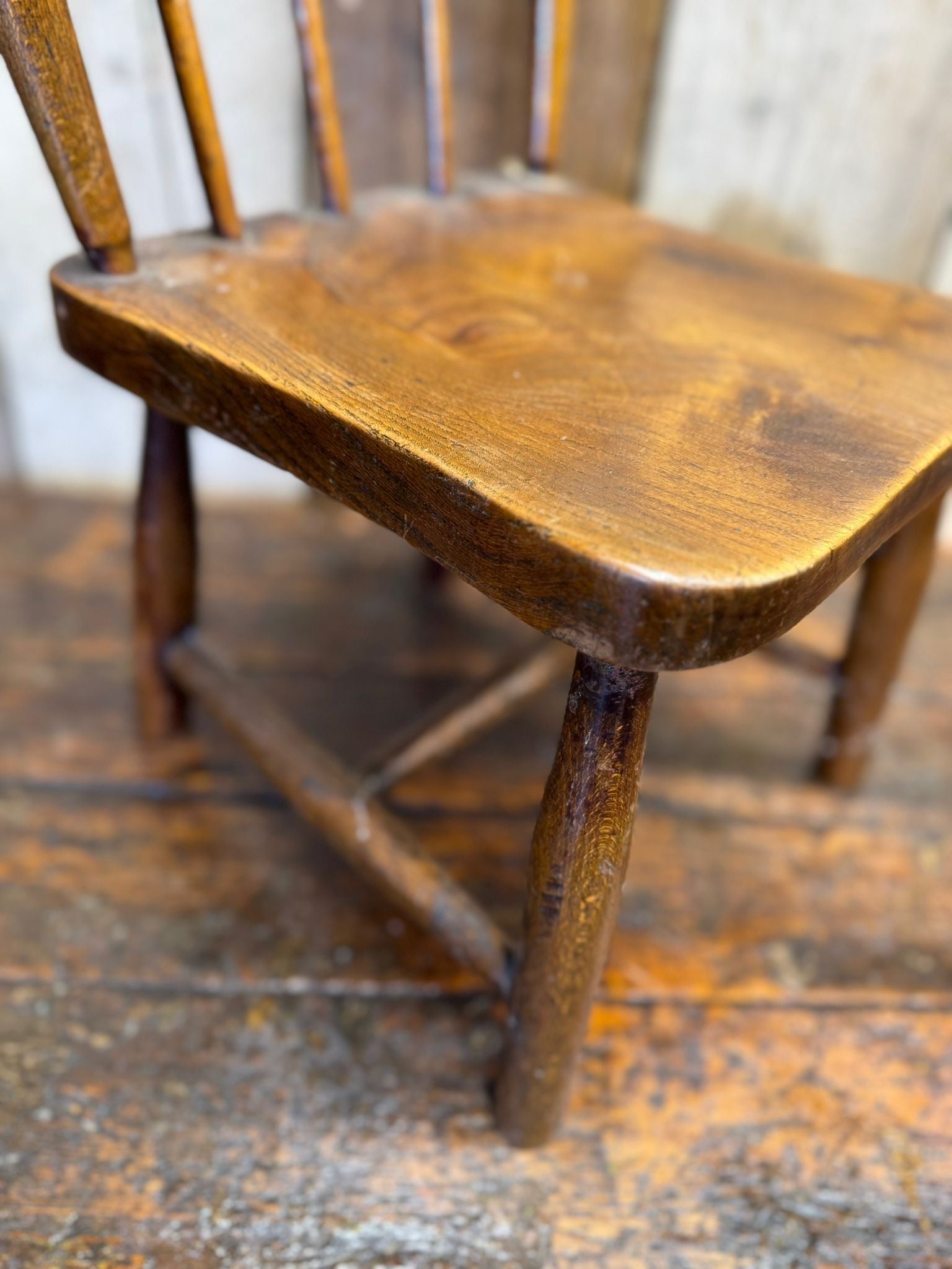 Antique childs chair with elm seat featuring a warm polished finish and slender wooden spindles for nursery use