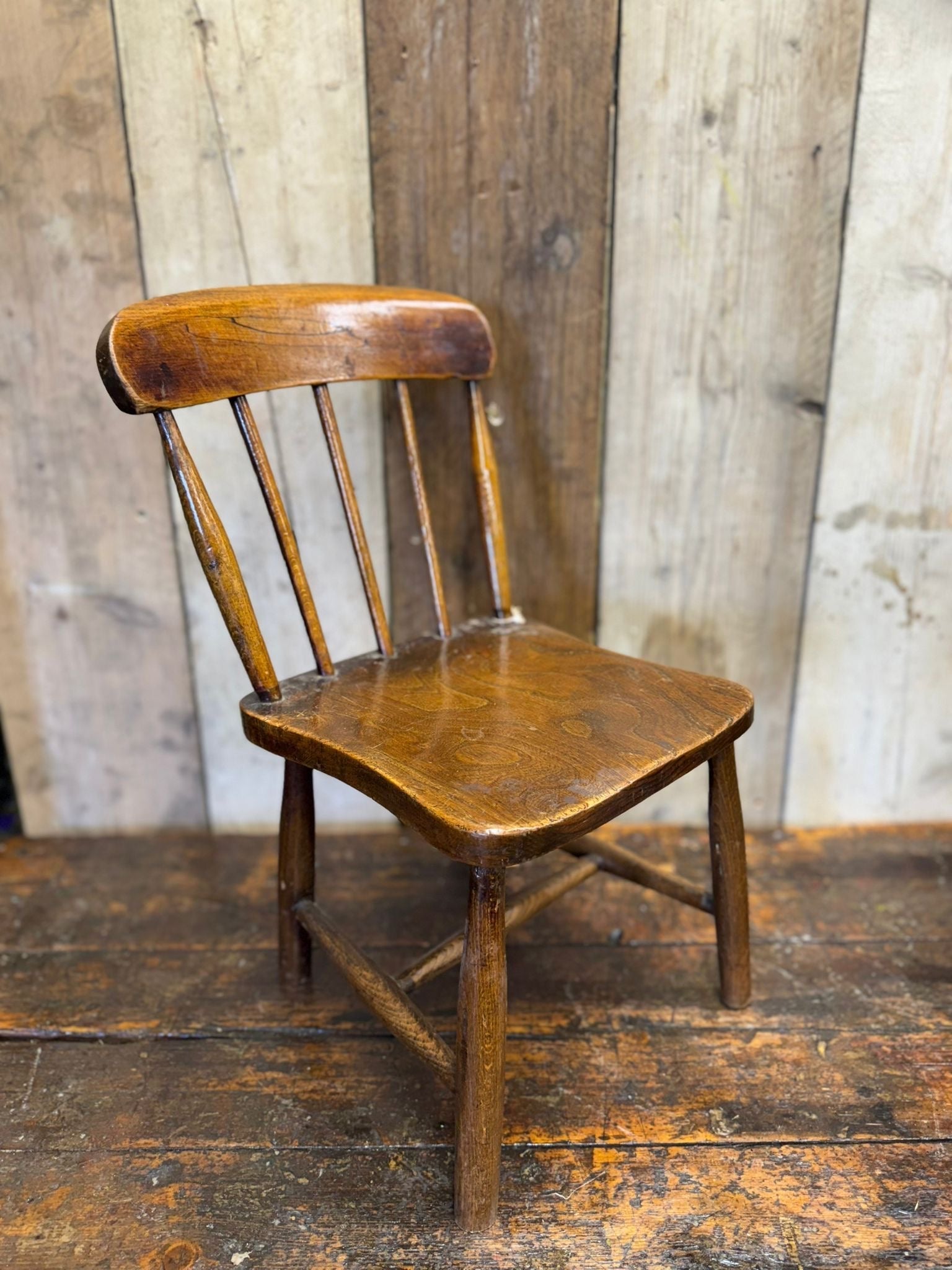 Antique child’s chair in dark brown wood with elm seat and curved spindle backrest for nursery or display use