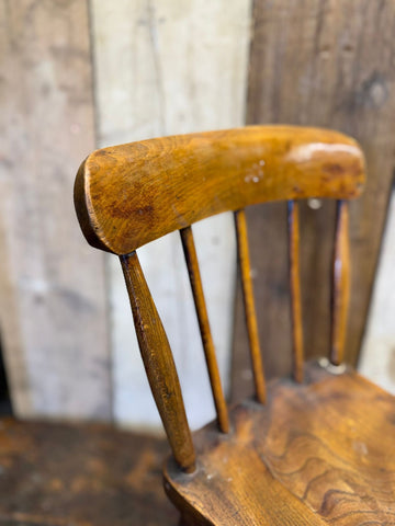 Antique child’s chair with elm seat featuring warm amber tones and curved wooden backrest with slender spindles