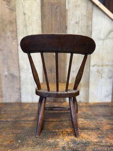 Dark brown antique child’s chair with curved backrest spindle design and oak seat perfect for nursery display