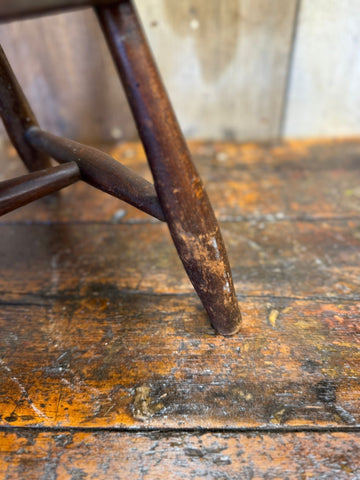 Dark brown wooden leg of antique child’s chair with oak seat showing rustic finish and visible wear
