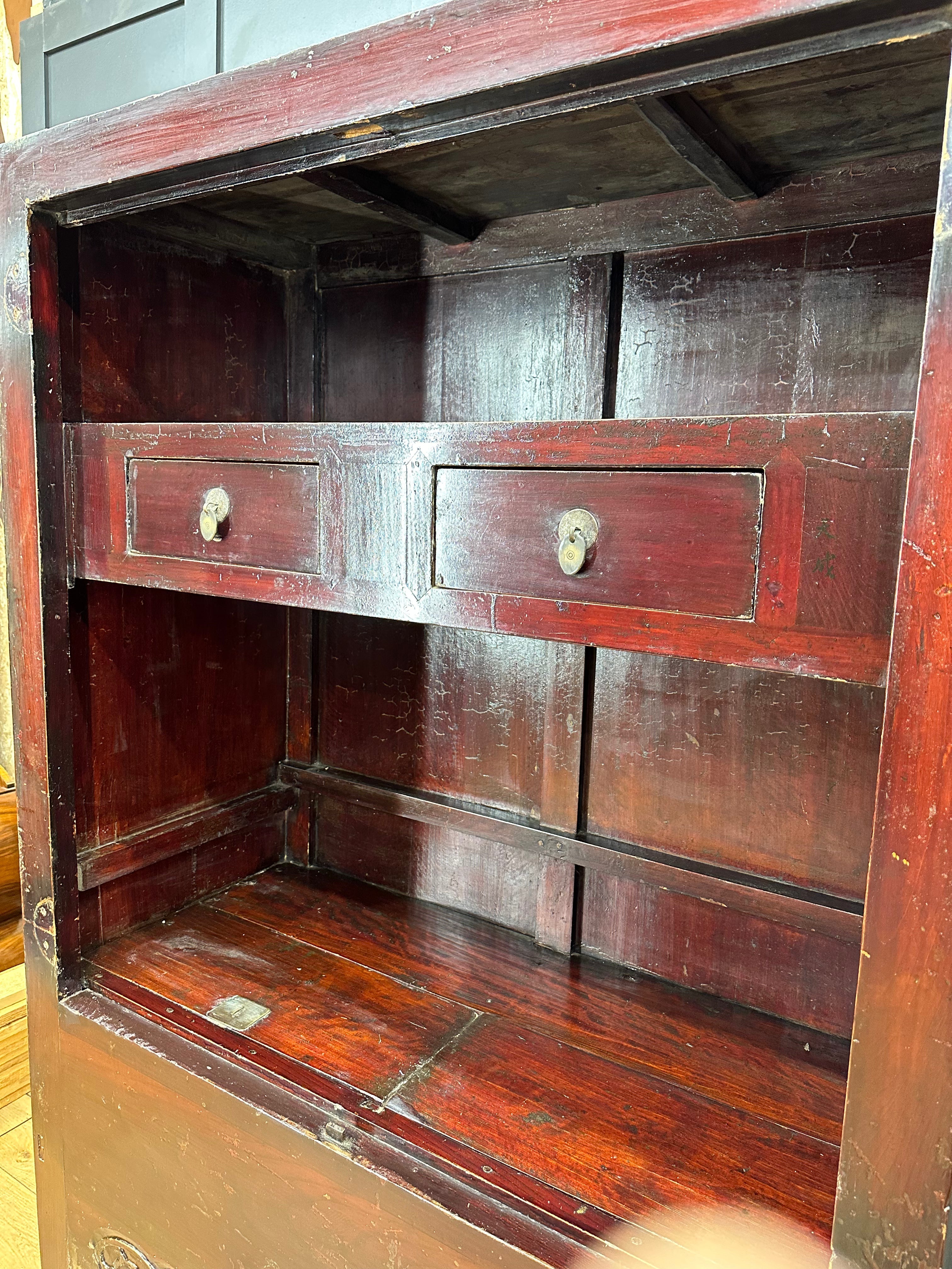 A dark reddish-brown wooden antique chinese wedding cabinet with two small drawers and round metal handles