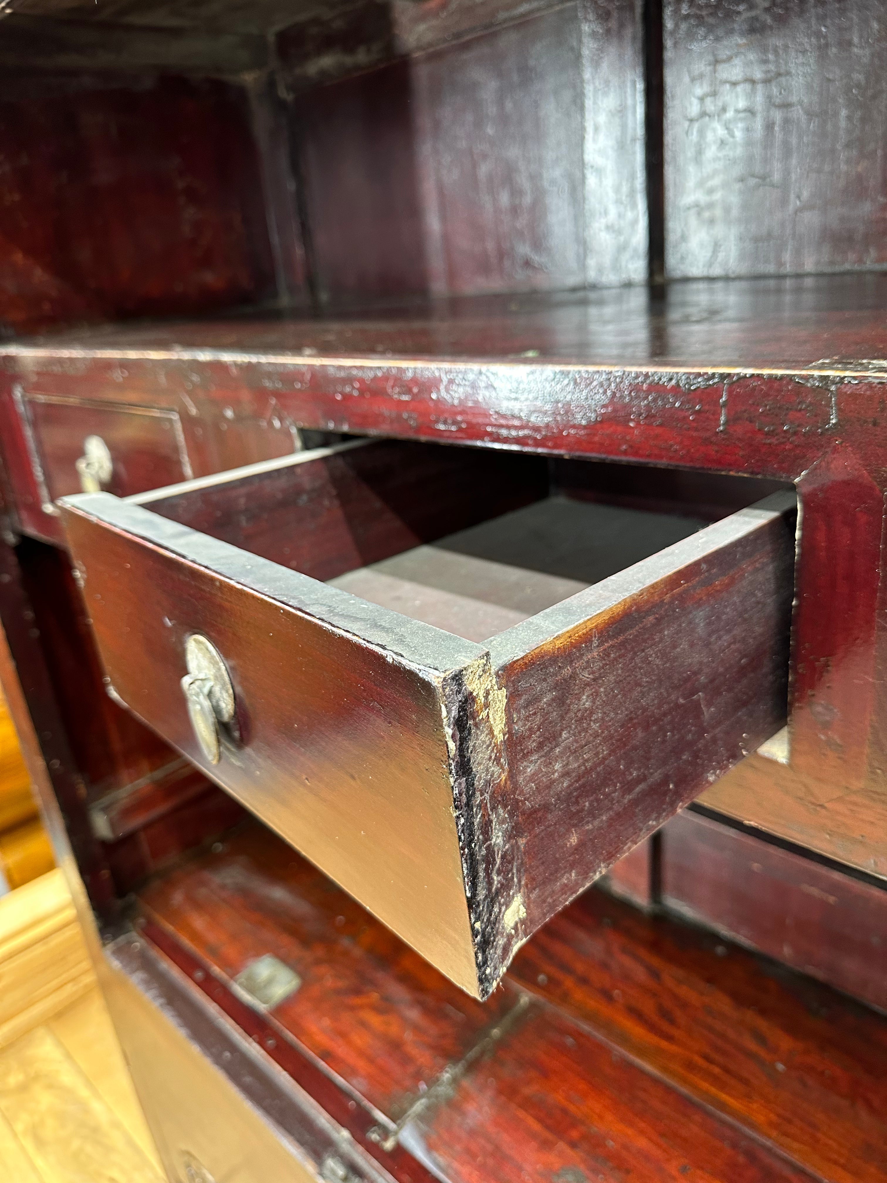A dark reddish-brown wooden antique chinese wedding cabinet drawer with tarnished metal pull handle showing age