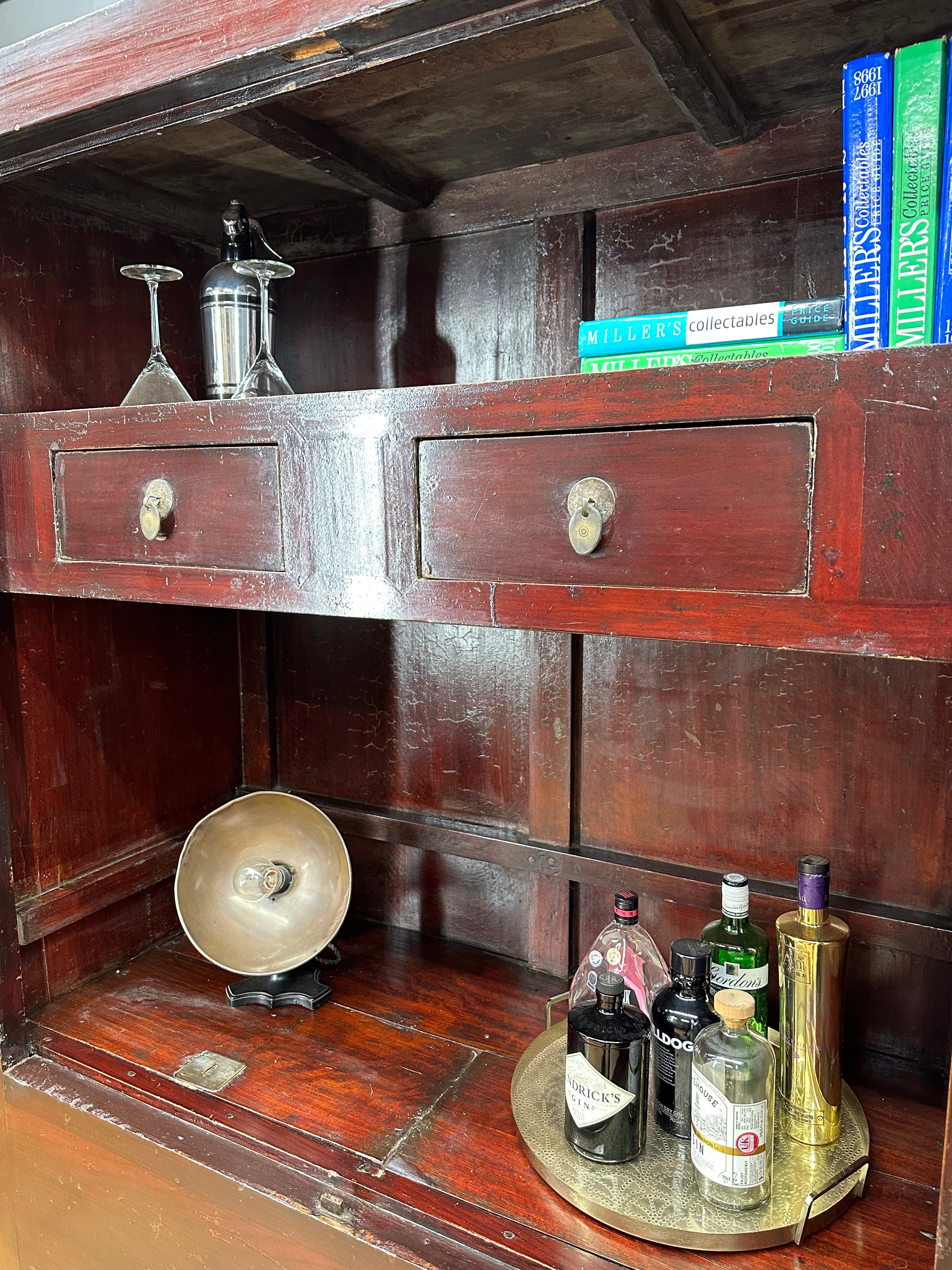 A vintage-style brass tray with liquor bottles and gold cocktail shaker inside an antique red wedding cabinet