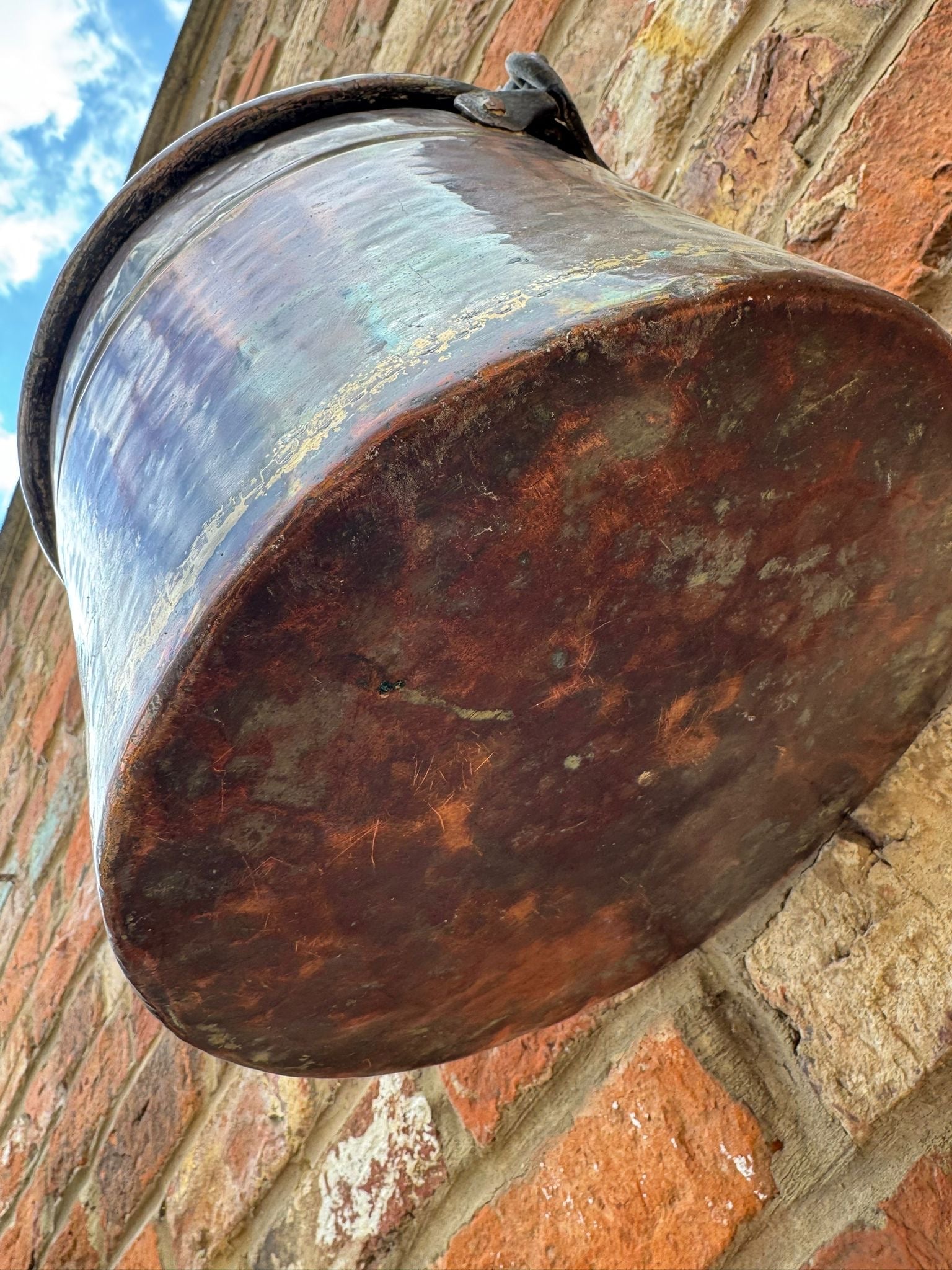Antique copper cauldron pot with riveted iron handle showing dark patinated surface and rust patches