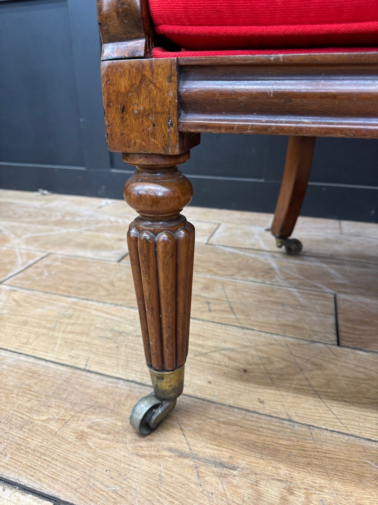 Antique mahogany armchair leg with red upholstered seat and brass-accented casters from victorian empire chair