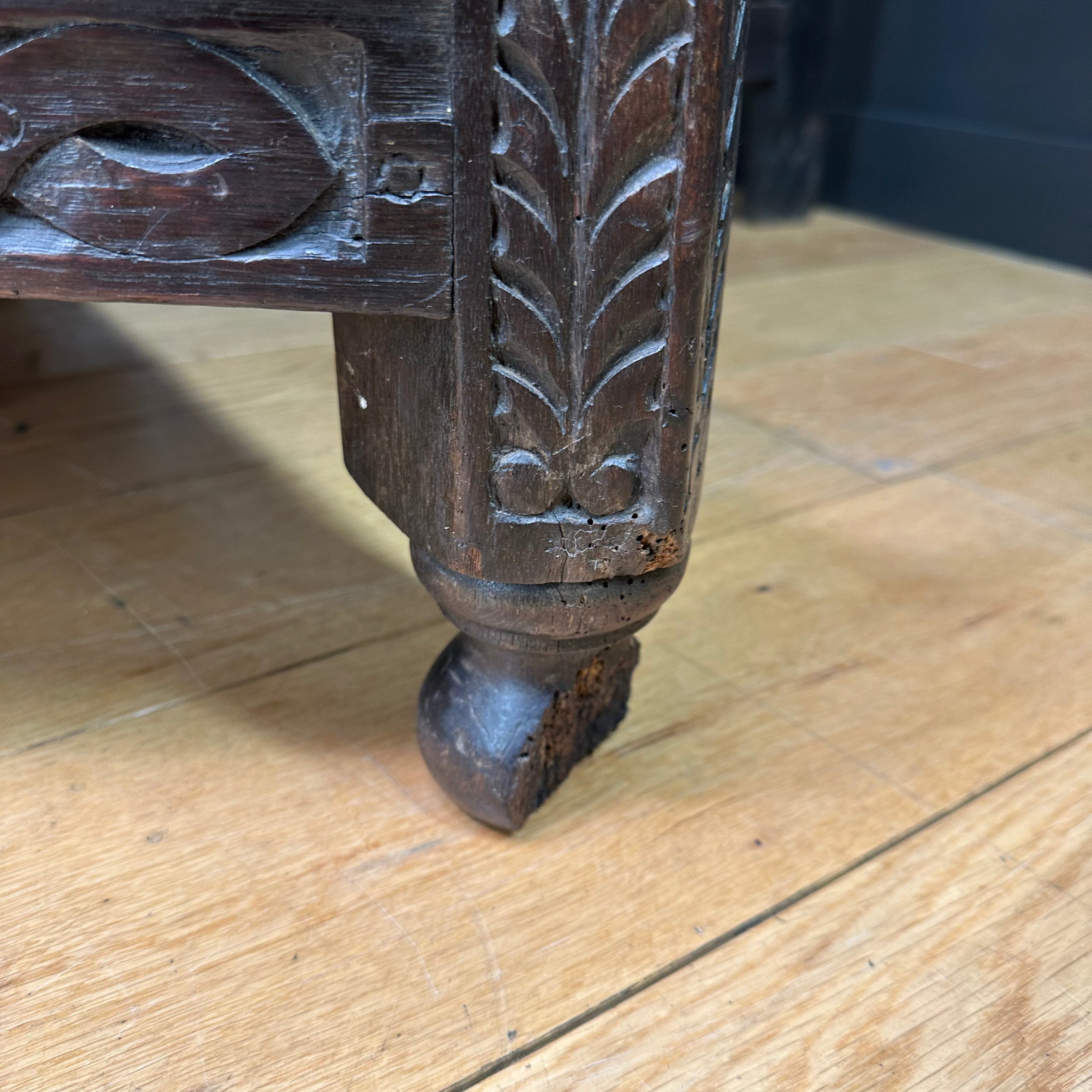 Dark brown carved wooden leg with leaf and scrollwork detailing on an antique oak credence table