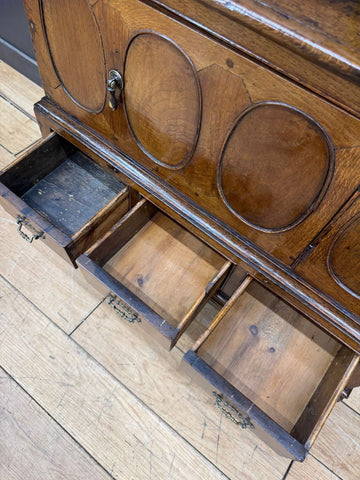 Antique oak cupboard with oval inlaid panels and brass hardware showing surface wear from the 18th century