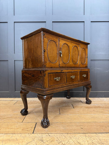 Antique oak cupboard with four oval-paneled doors and three drawers with brass handles showing surface wear from 18th century
