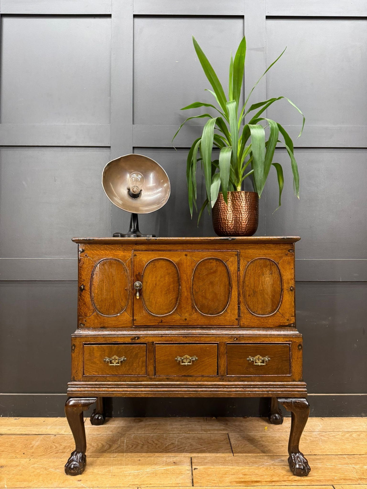 Antique oak sideboard with brass hardware and oval panel doors showing surface wear on 18th century oak cupboard
