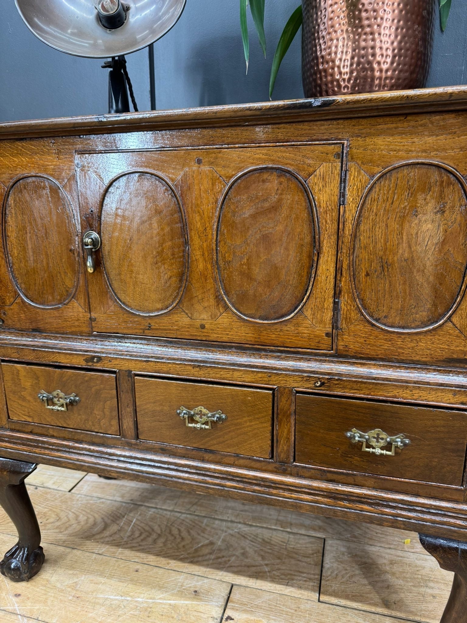 Antique oak sideboard with four oval-panelled doors and ornate brass handles showing slight surface wear from 18th century oak cupboard