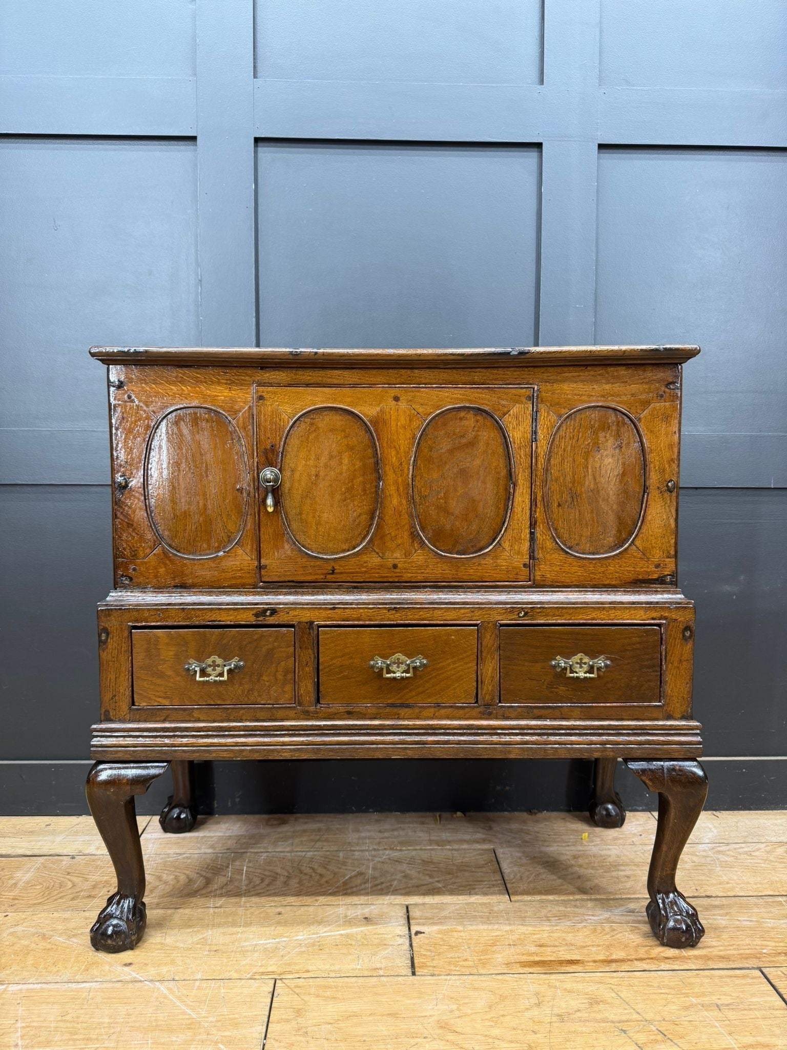 Antique oak sideboard with four oval-panelled doors and ornate brass handles showing surface wear from 18th century oak cupboard