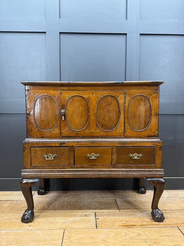 Antique oak sideboard with four oval-panelled doors and ornate brass handles showing surface wear from 18th century oak cupboard