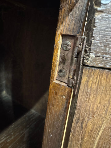 Rusty metal hinge on dark wood frame showing surface wear of 18th century oak cupboard sideboard