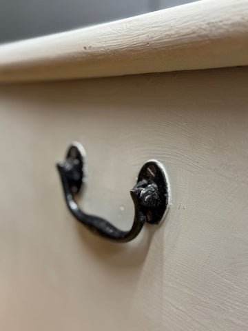 Black wrought iron drawer pull with ornate curve on light beige antique painted blanket chest for shoe storage and more