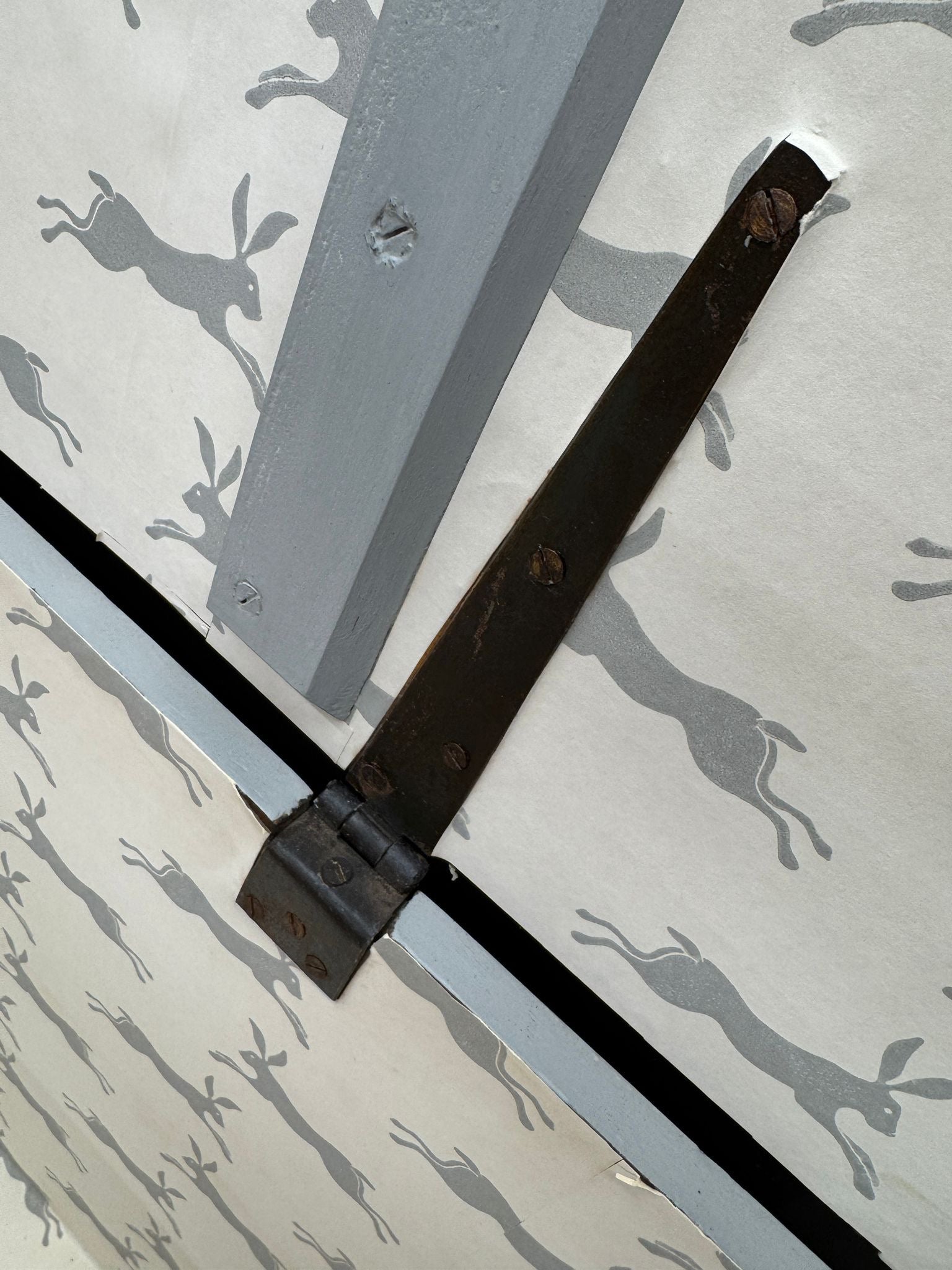 Dark weathered metal hinge with rust on an antique painted blanket chest for shoe storage and tv stand use
