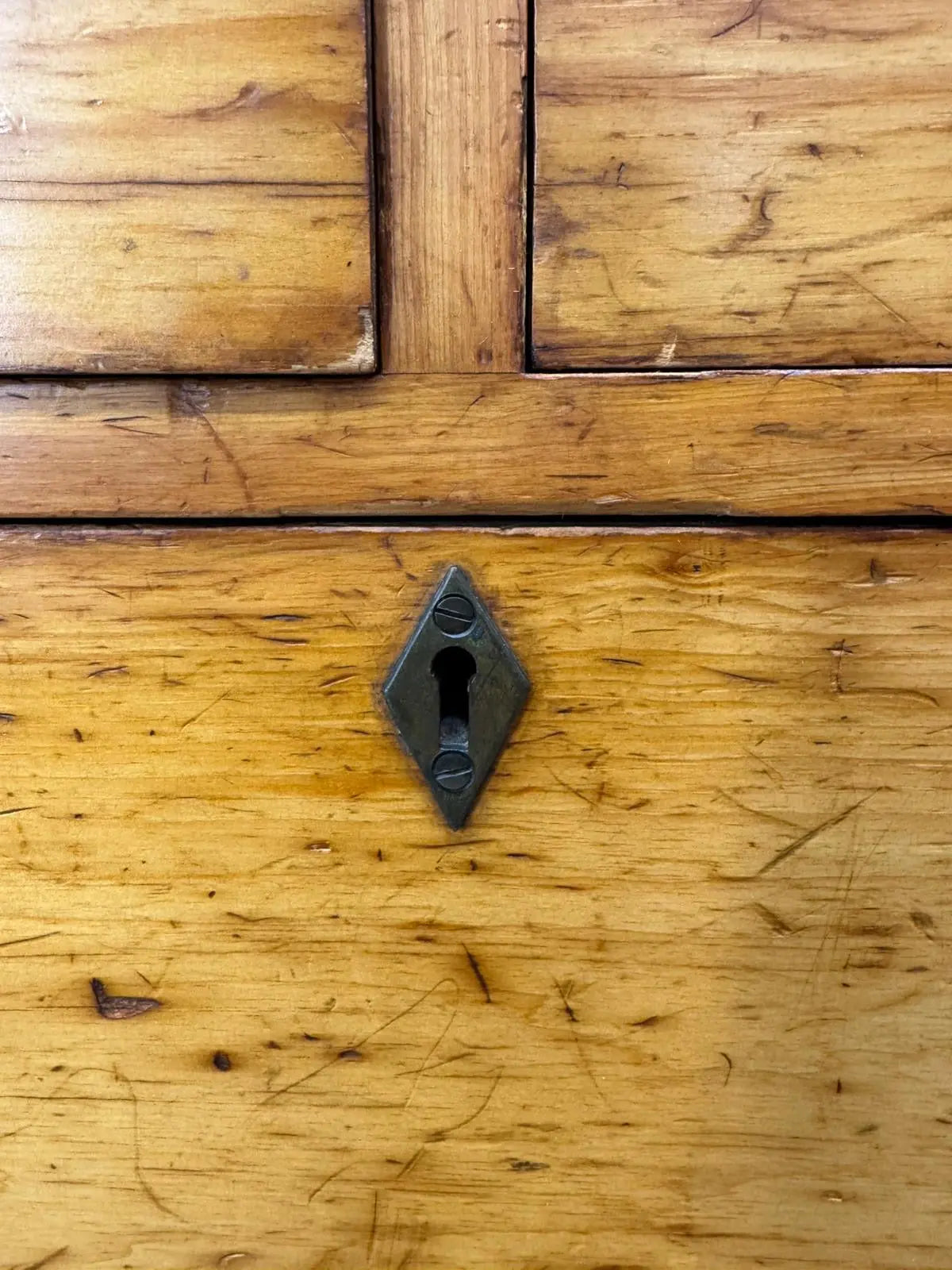 A dark diamond shaped metal keyhole with vintage finish on an antique pine chest for country house storage
