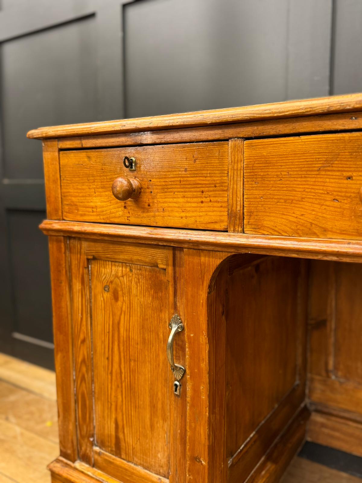Antique pine pedestal desk with two drawers and a cupboard door featuring brass hardware in oak finish