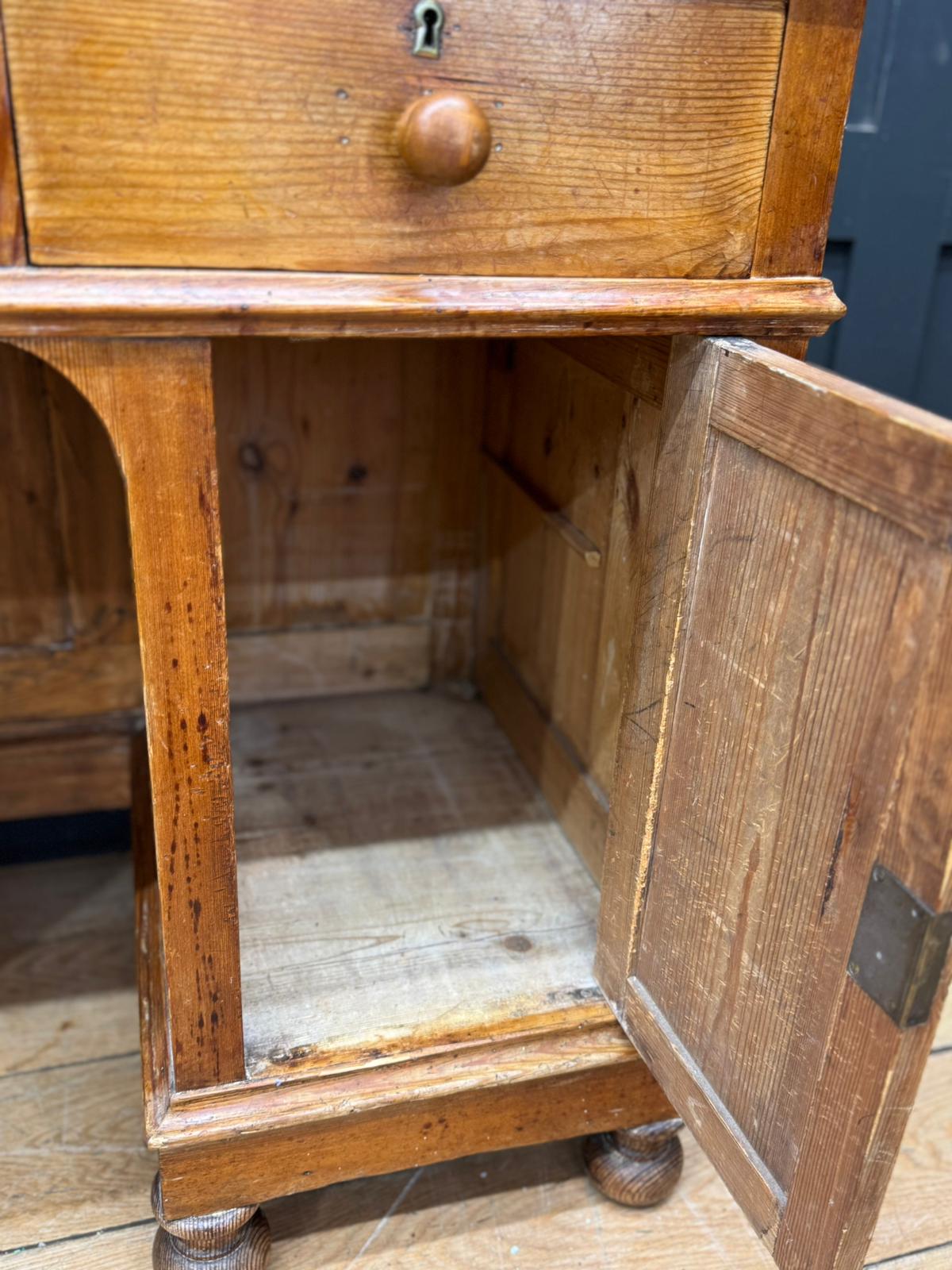 Antique pine pedestal desk with turned legs open cupboard and single drawer featuring round knob and visible wood grain