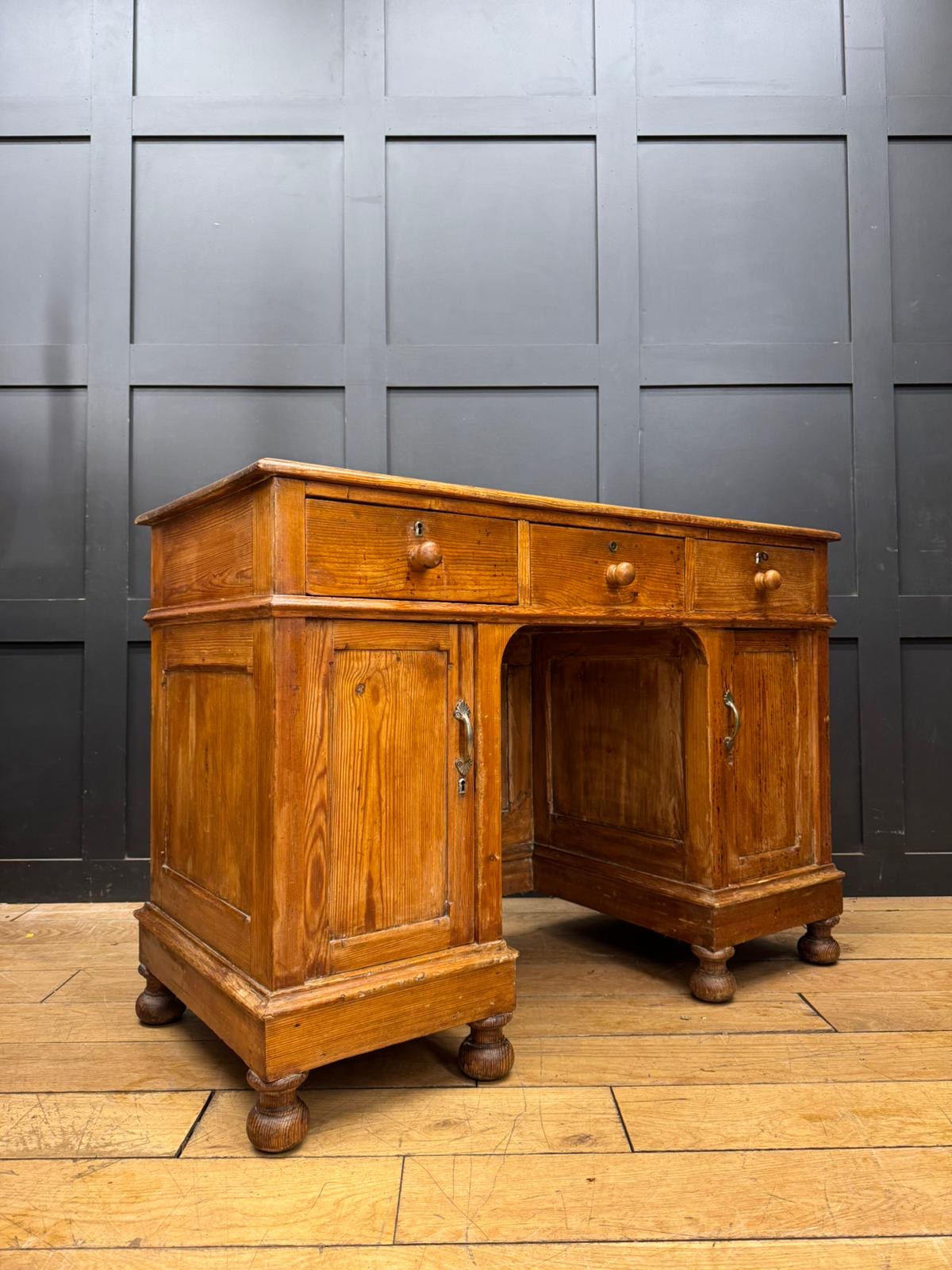Antique pine pedestal desk with three drawers, two cupboards, turned wooden legs, and brass hardware in oak finish