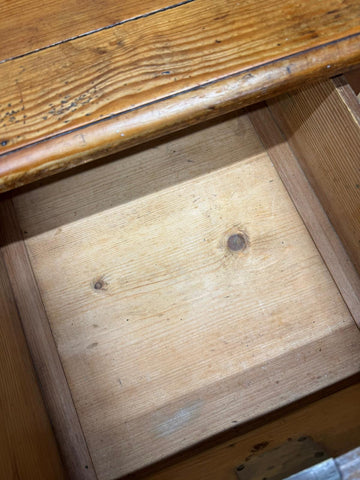 A rustic wooden drawer with warm natural finish and visible grain in an antique pine pedestal desk dressing table