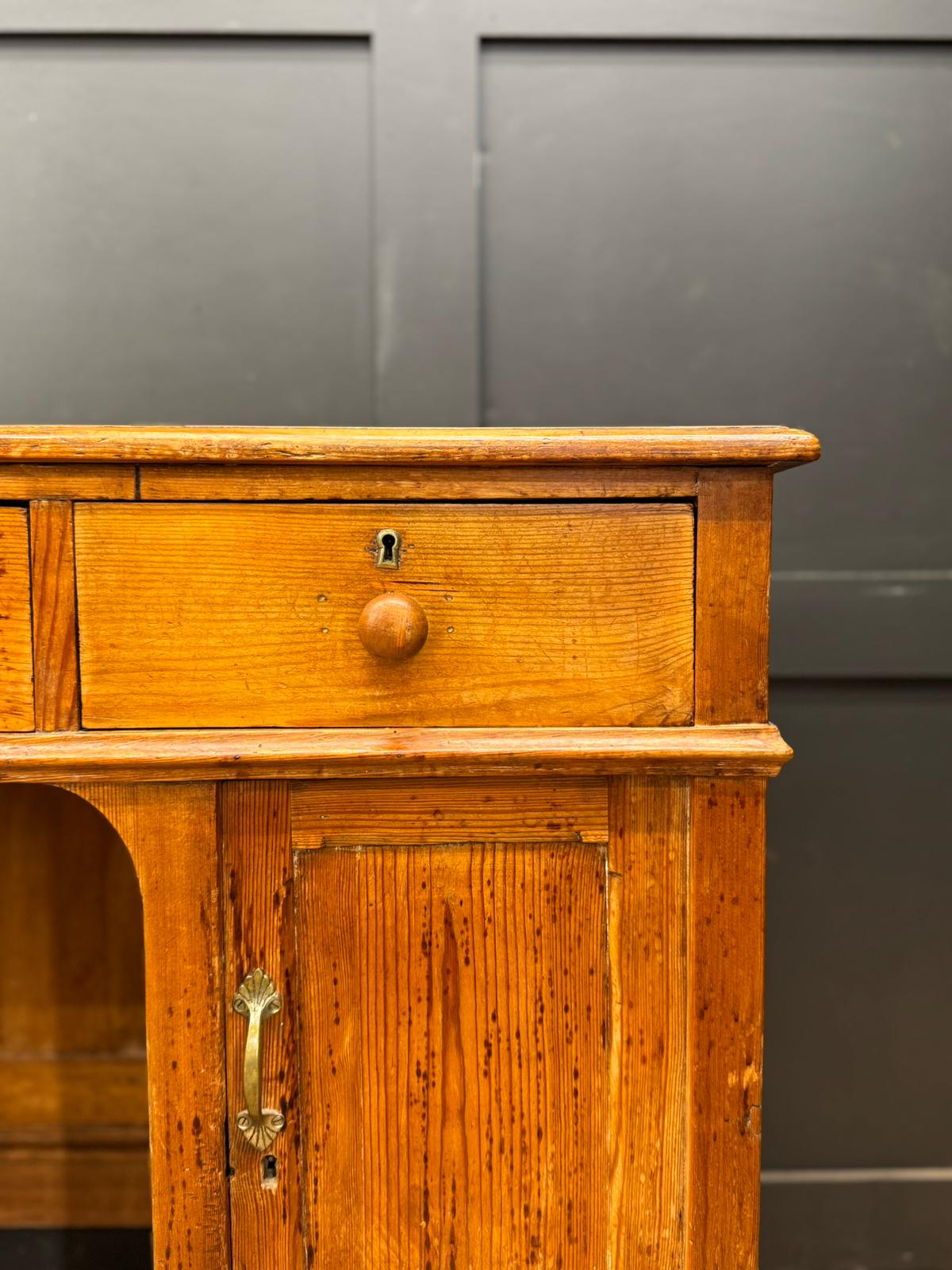 Antique pine pedestal desk dressing table with warm amber finish, single drawer, door, and brass hardware