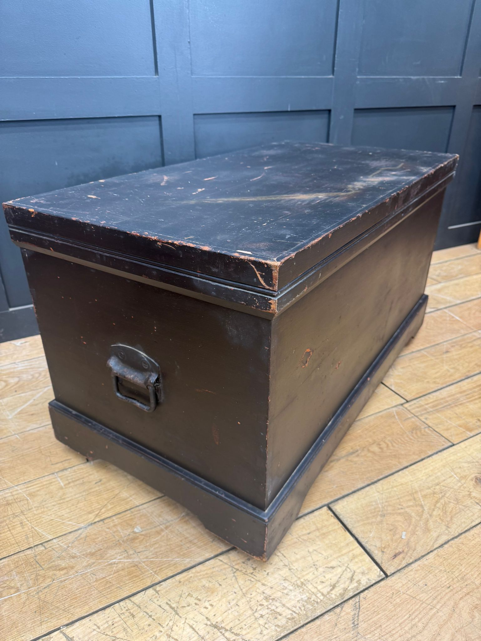 Black wooden chest with worn finish and metal handle used as an antique pine trunk or blanket box coffee table